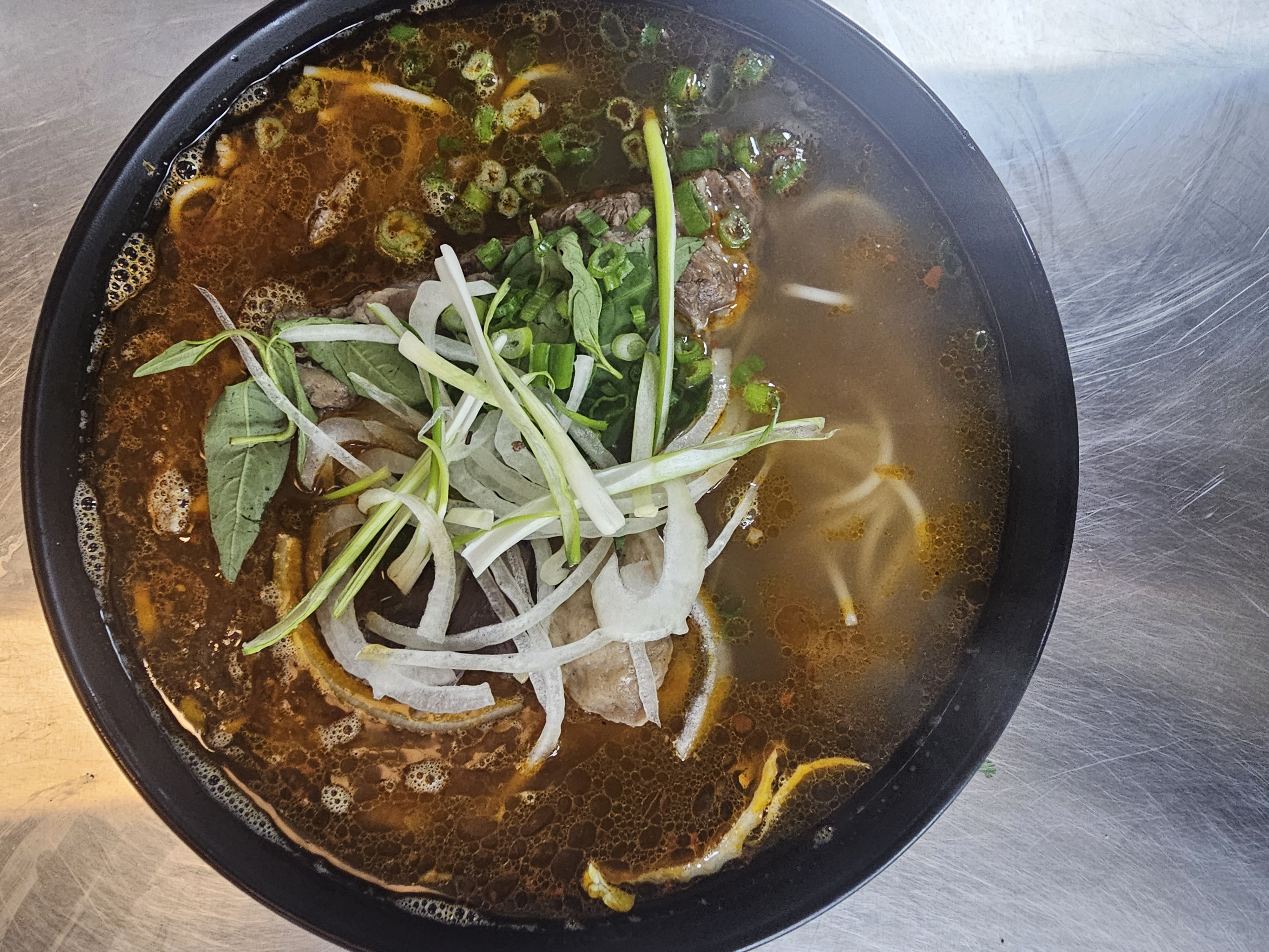 Steaming bowl of Bún Bò Huế — spicy Vietnamese beef noodle soup with lemongrass broth